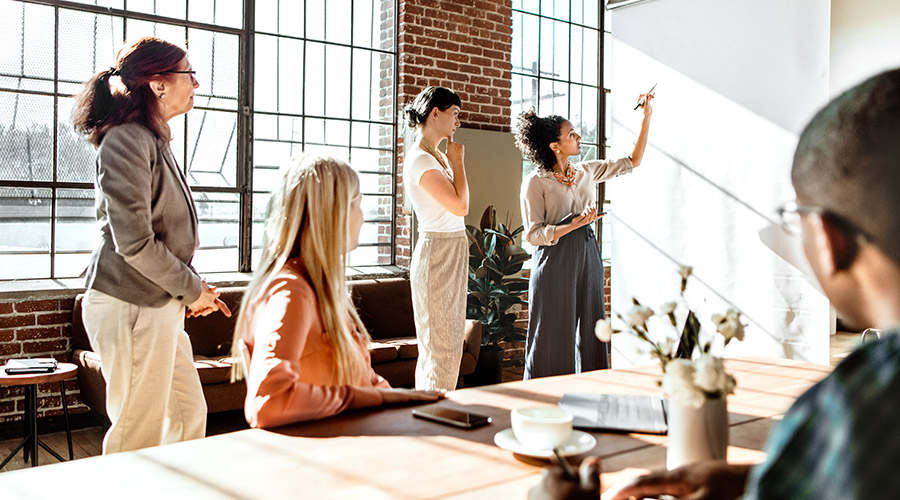 A team of people standing and sitting in a conference room looking at and writing on a whiteboard.